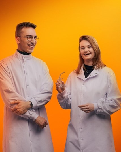 Turuncu arka plan önünde gülümseyen iki bilim insanı