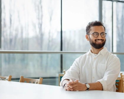 Masasında gülümseyerek oturan gözlüklü bir erkek çalışan